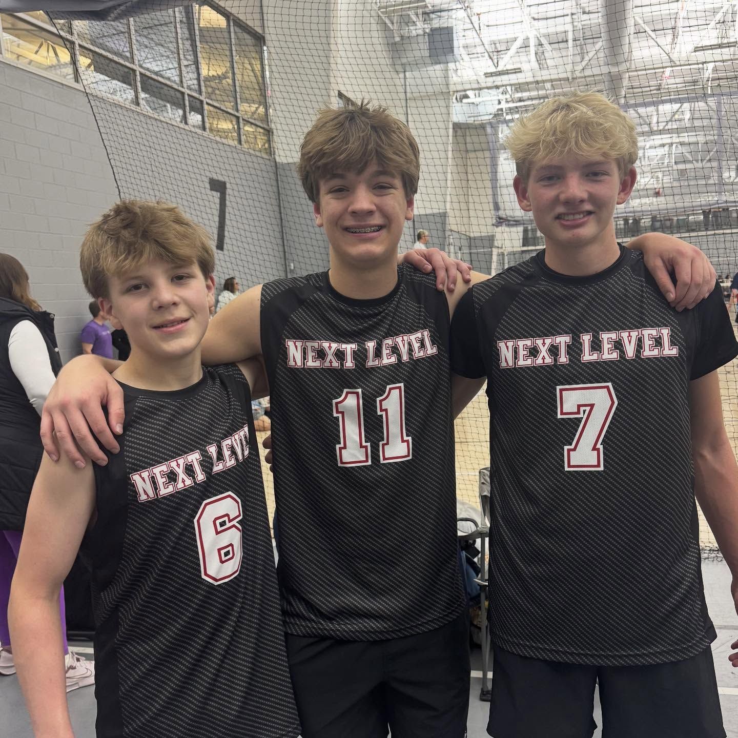 Volleyball game in an indoor dome; players in action, hitting and setting the ball. Green turf, blue ceiling.