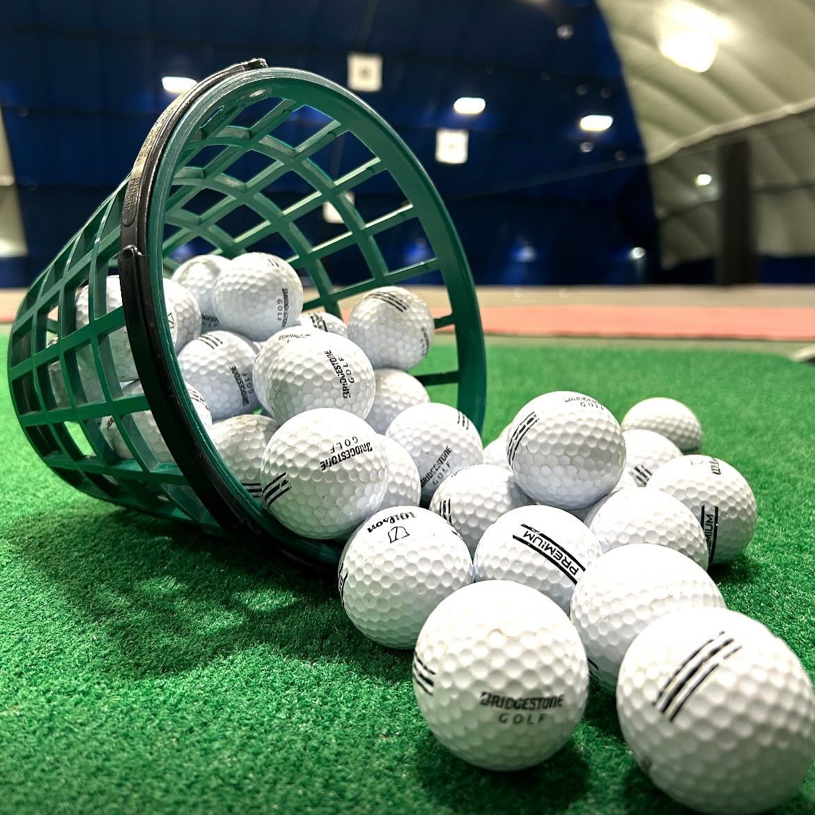 Golf balls scattered on artificial green grass inside a dome-shaped indoor driving range.
