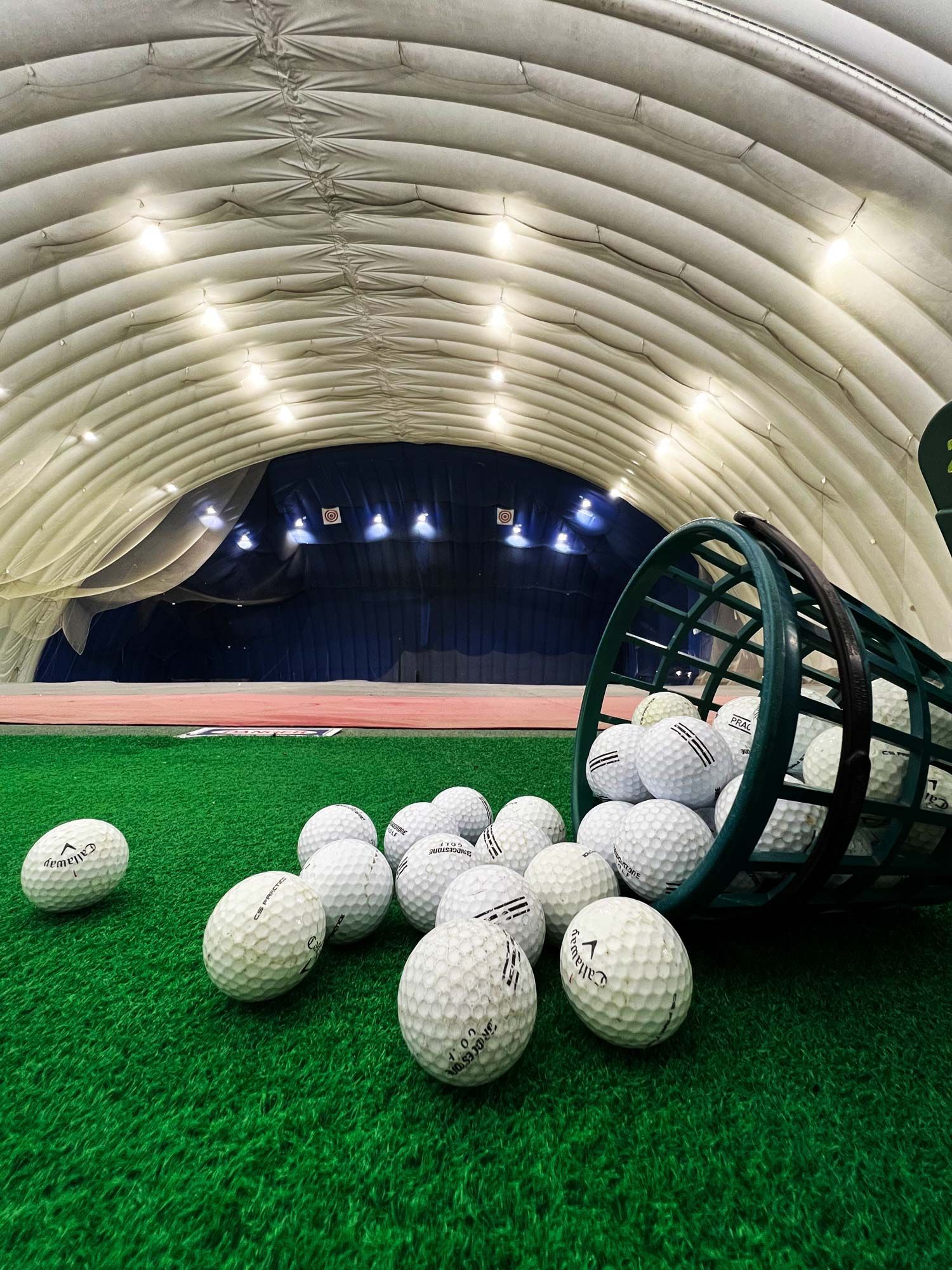 A bunch of golf balls are spilling out of a basket on the grass.