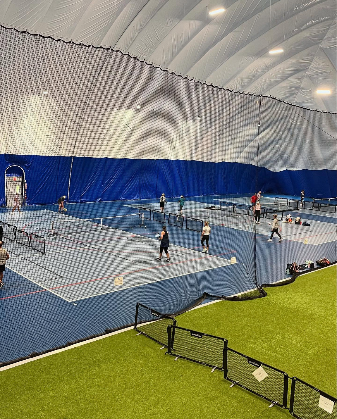 Indoor sports court with pickleball nets under a dome-shaped white ceiling and blue and grey floor.