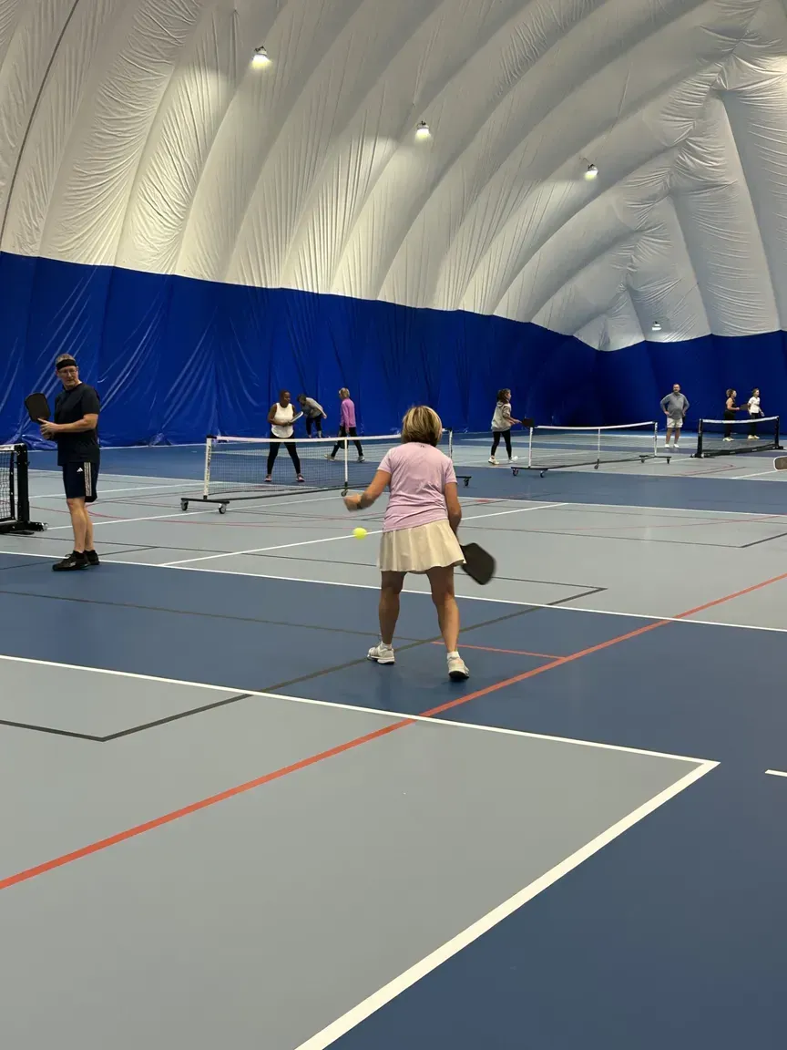 A person swinging a bat at a yellow softball inside a batting cage.