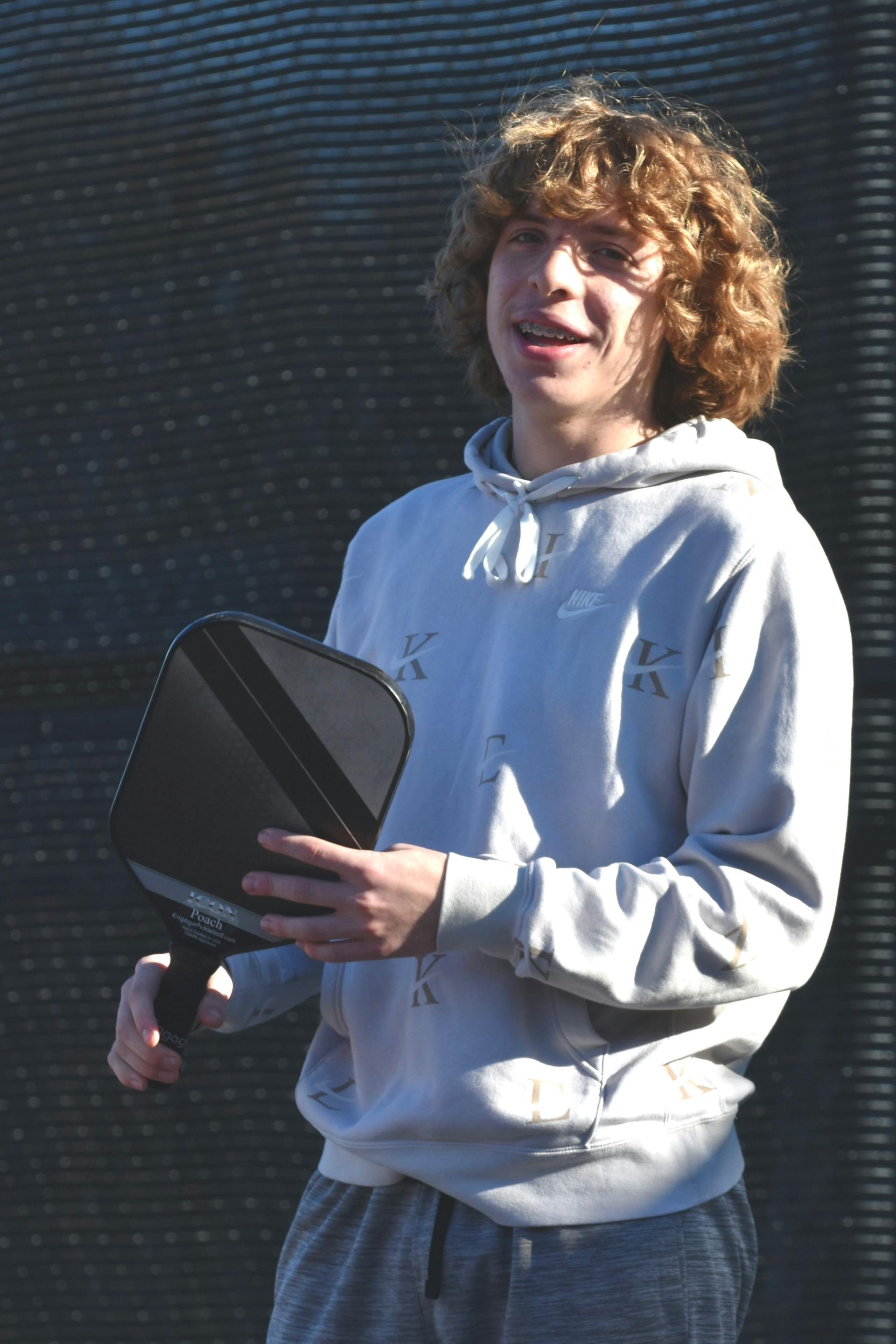 A young man with curly hair is holding a tennis paddle