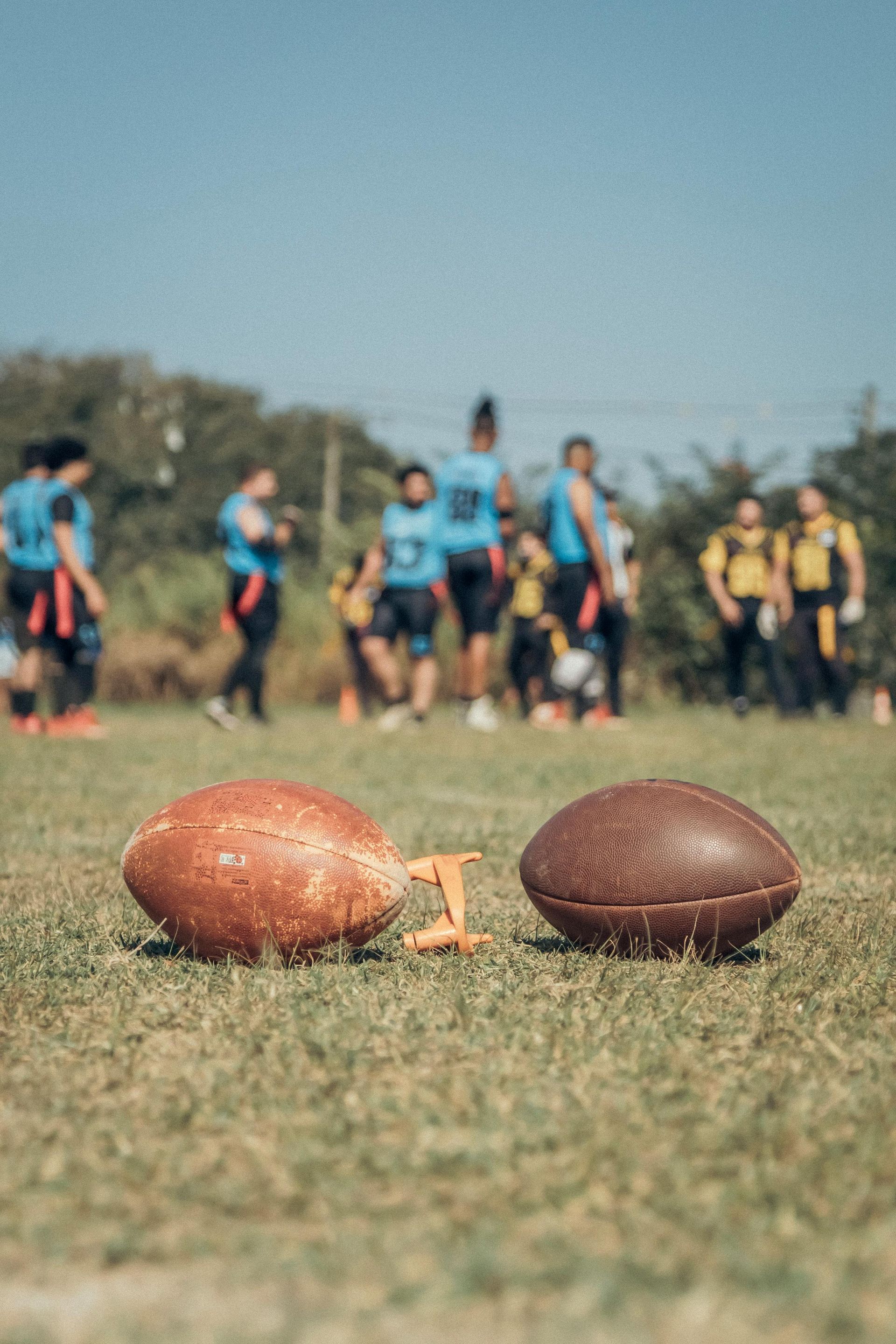 Two footballs are sitting on top of a lush green field.