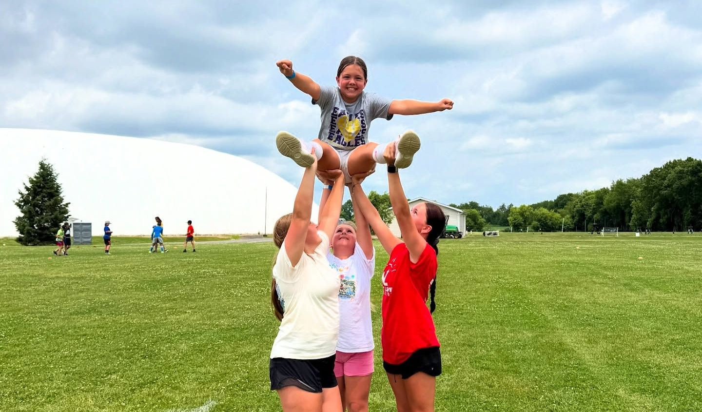 An aerial view of a white dome structure with a building and parking lot, set on a green lawn.