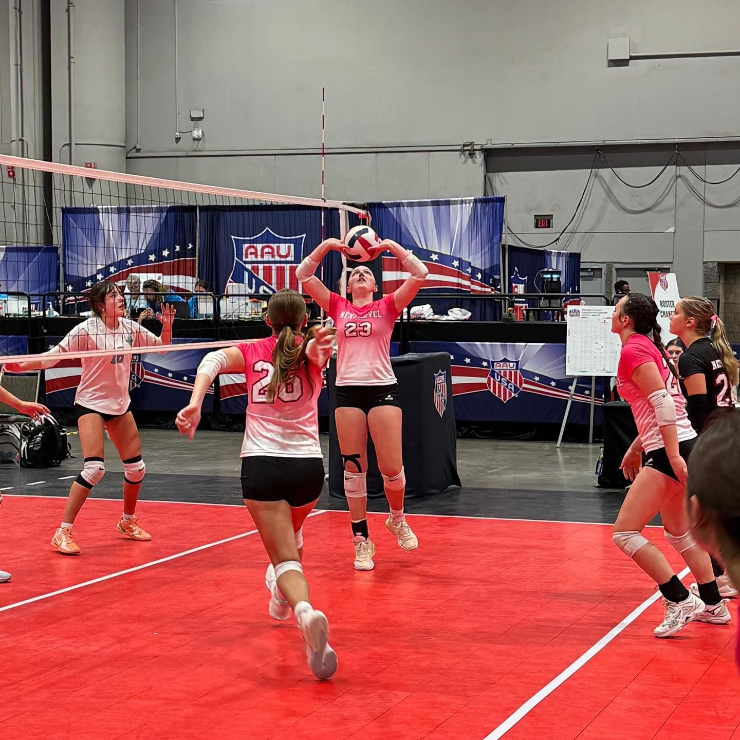 Volleyball team poses on court; nine young women in black and white uniforms; an American flag is in the background.