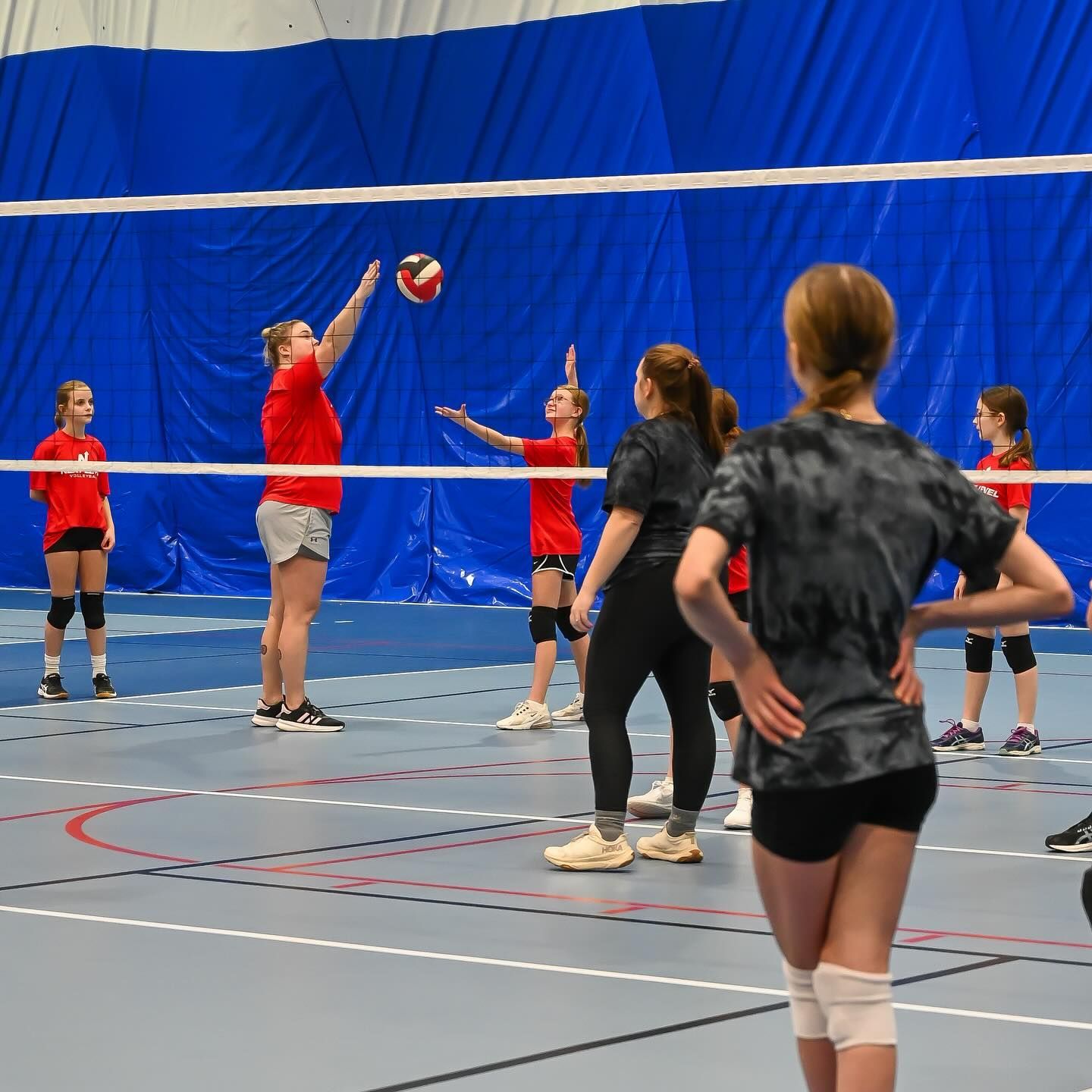 Volleyball player spikes the ball mid-air. Red and black uniforms on a red court.