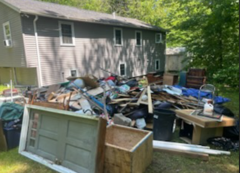 Backyard with a large pile of trash and debris next to a two-story house.