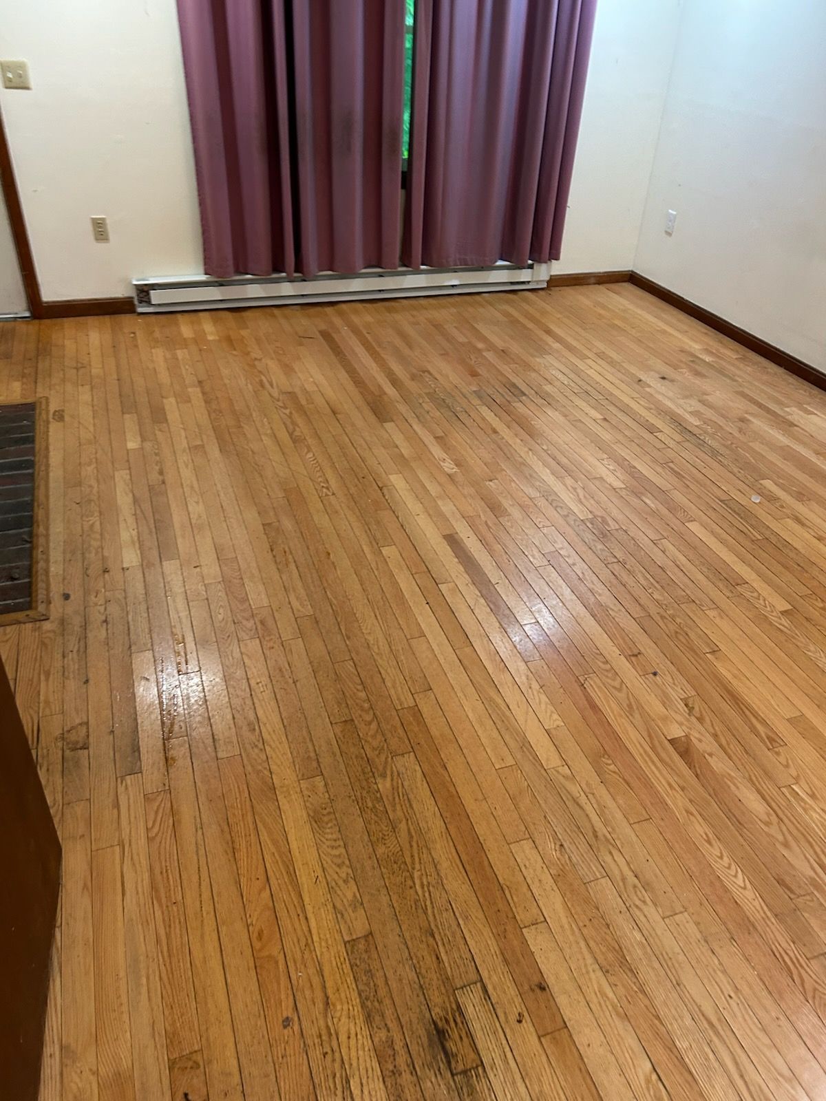 Hardwood floor in a room with a radiator, window with pink curtains, and a door.