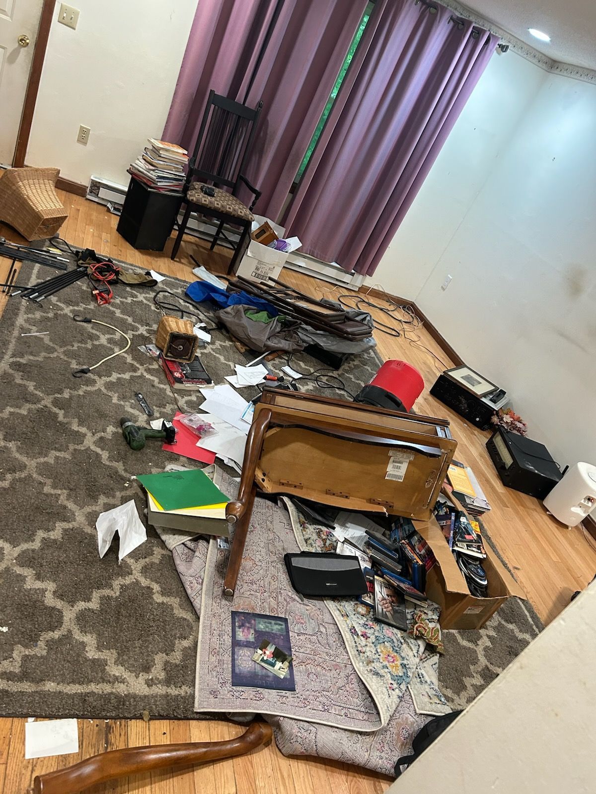 Messy room with scattered items on a patterned rug, including furniture, papers, and other debris.