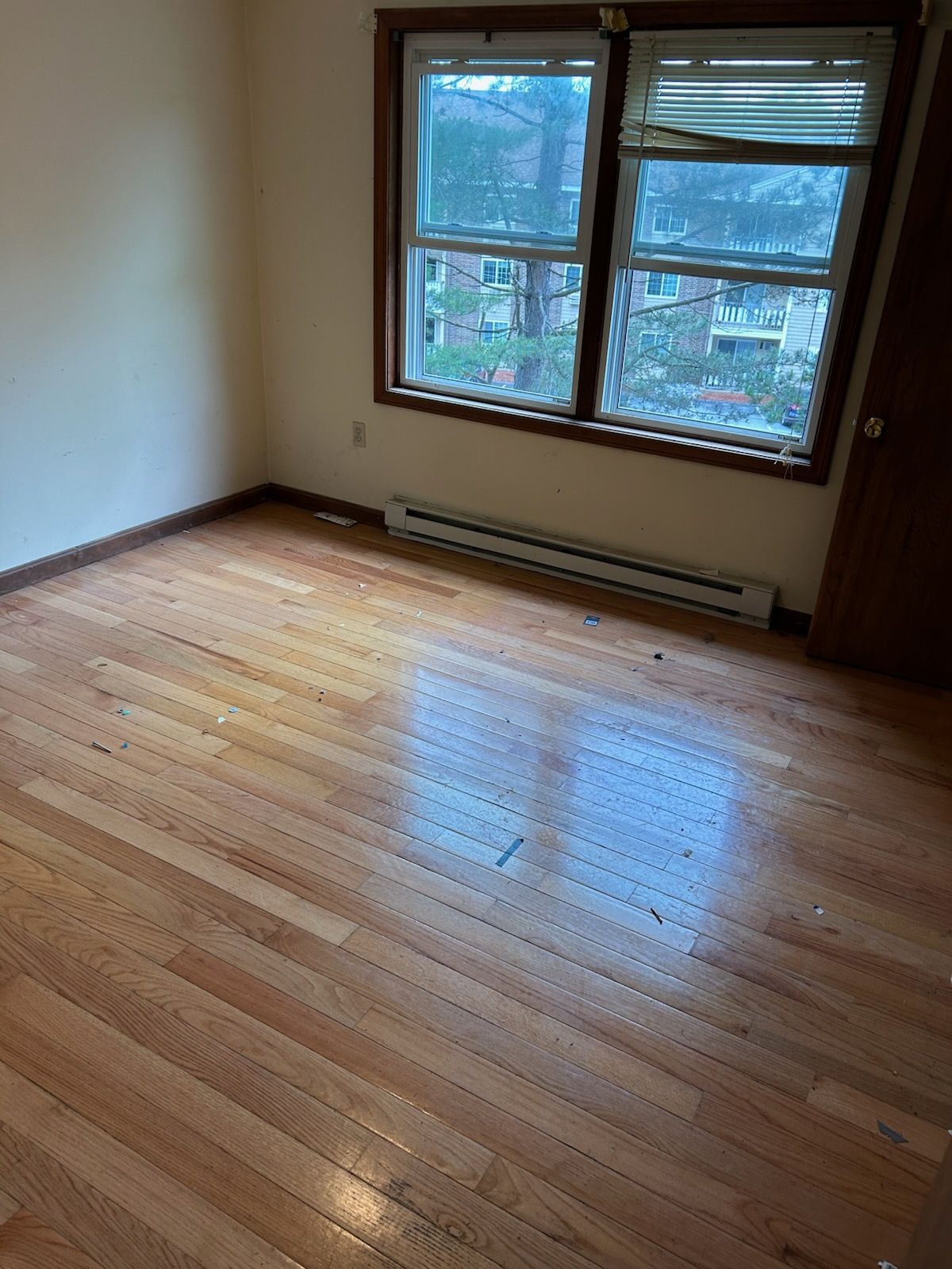 Empty room with hardwood floor, window, and baseboard heater.
