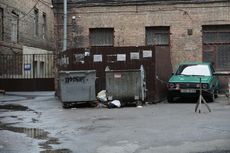 Green car parked next to dumpsters in a brick alley.