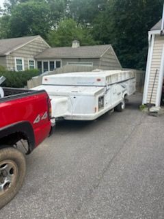 Red truck towing a white pop-up camper on a paved driveway near houses and trees.