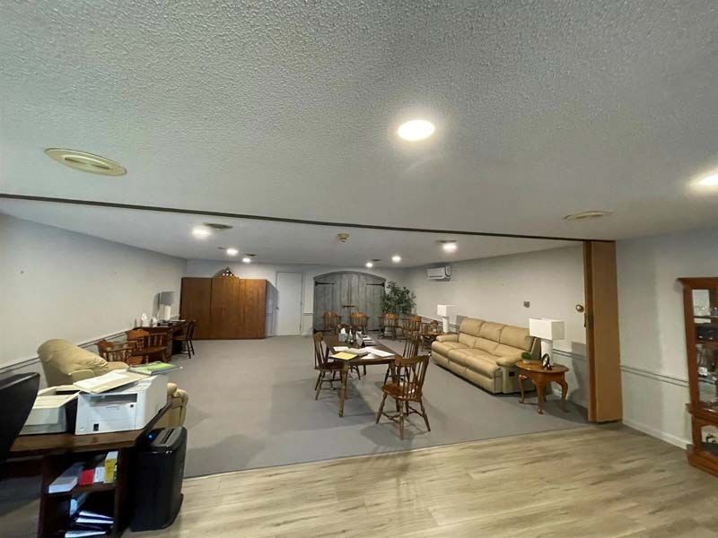 Large, open room with seating, tables, and cabinets; neutral colors and recessed lighting.