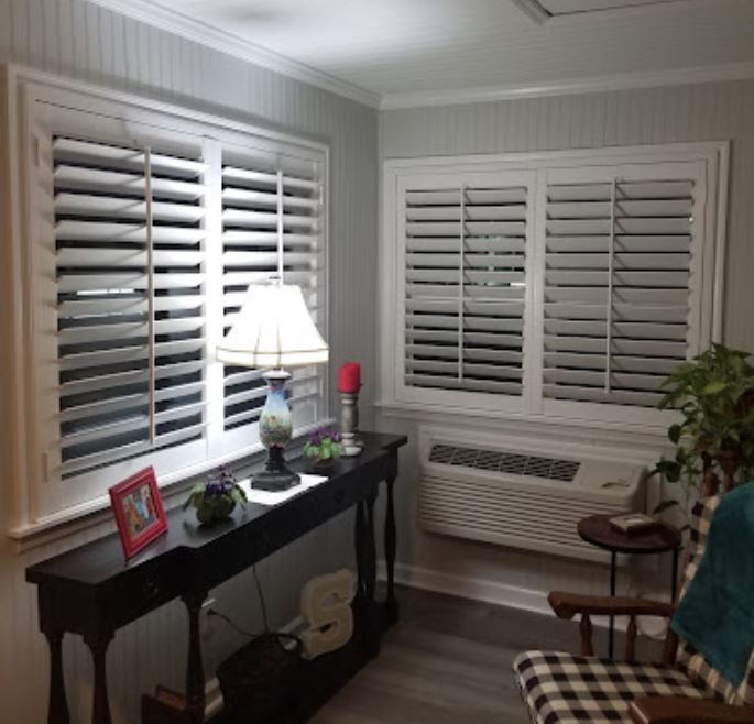 A living room with a table , chair , lamp and shutters on the windows.