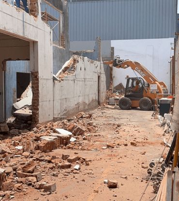 Sitio de construcción, una minicargadora Case demoliendo un muro; escombros esparcidos en el suelo.