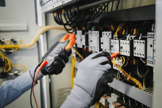 Una persona con guantes prueba el cableado eléctrico en un gabinete con un multímetro.