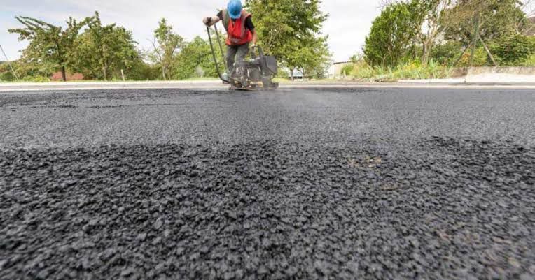 Persona que utiliza una máquina para aplicar sellador en una carretera recién pavimentada.
