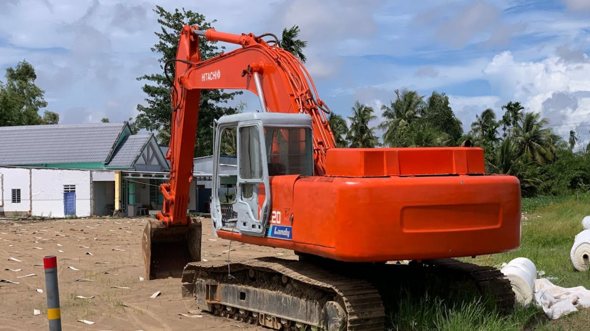 Excavadora Hitachi naranja en un sitio de construcción; edificio al fondo.