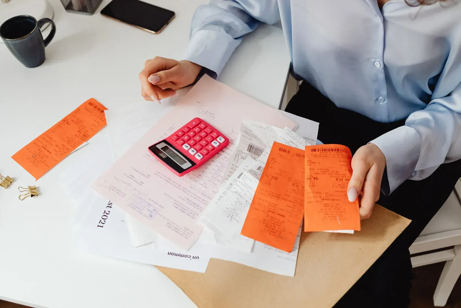Woman at desk sorting through receipts and documents, with calculator and phone visible.