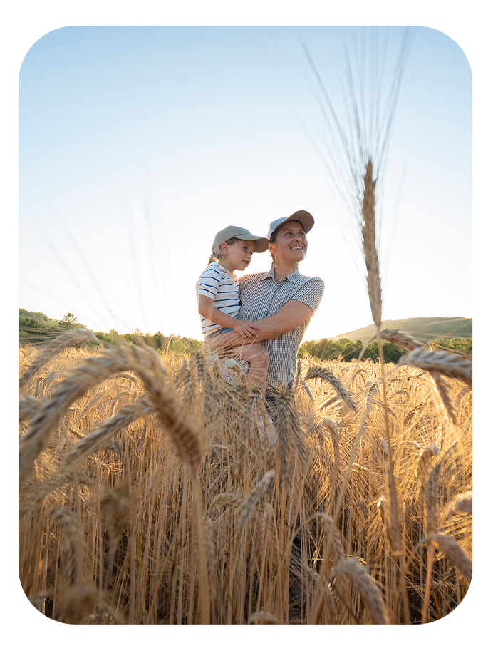 Person holding a child, standing in a wheat field, looking up at the sky.