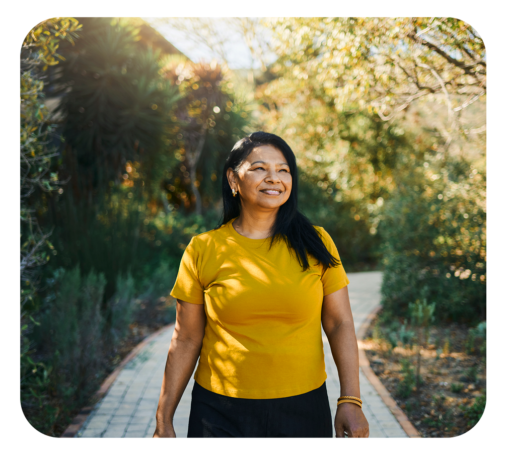 Woman smiles while walking on a path in a park, wearing yellow shirt.