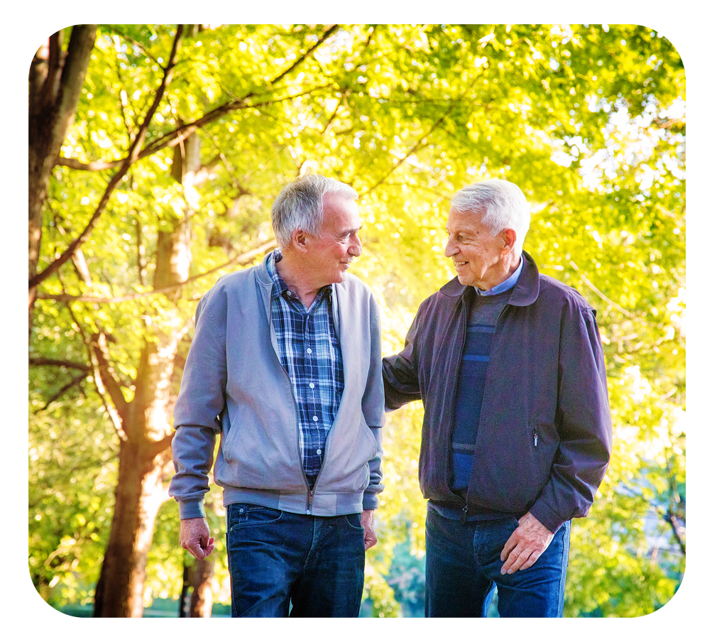 Two men walking and talking in a park; one has an arm on the other's shoulder; trees in the background.