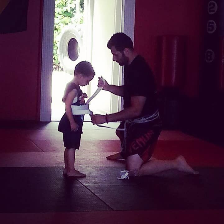 A man kneeling next to a little boy who is wearing shorts that say venum