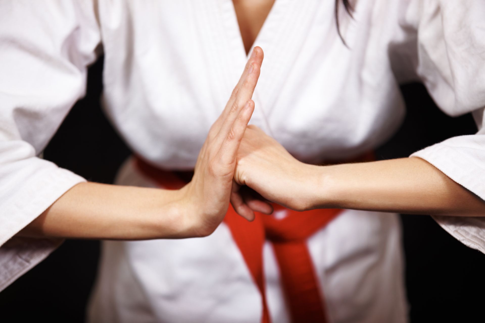A woman in a white karate uniform with a red belt holds her hands together.