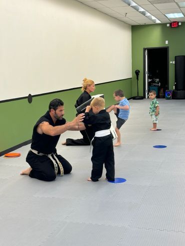 A man is kneeling down to help a young boy in a karate class.