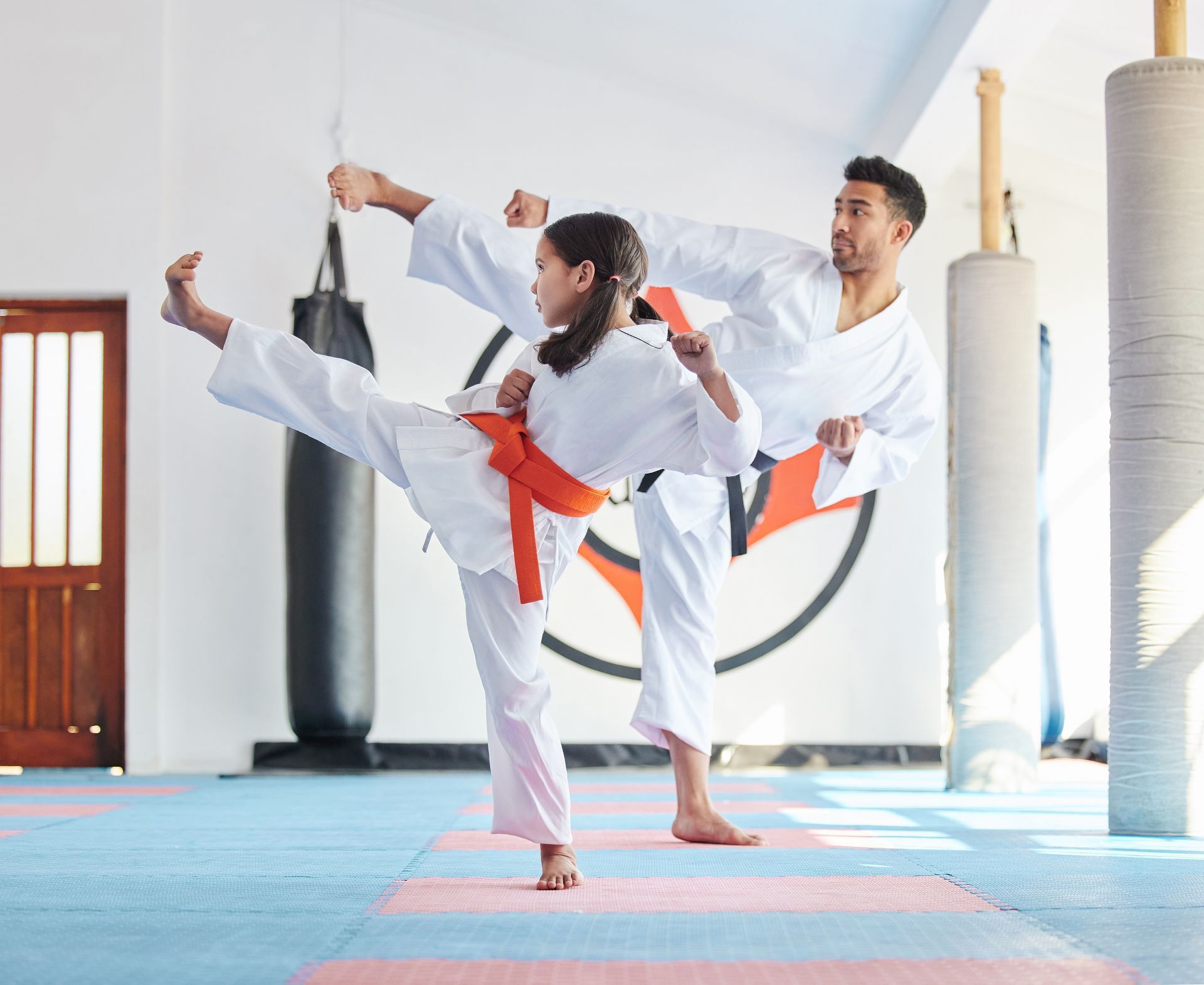 A man and a girl are practicing karate in a gym.