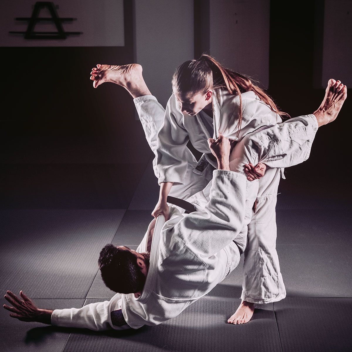 A man and a woman are practicing judo on a mat.