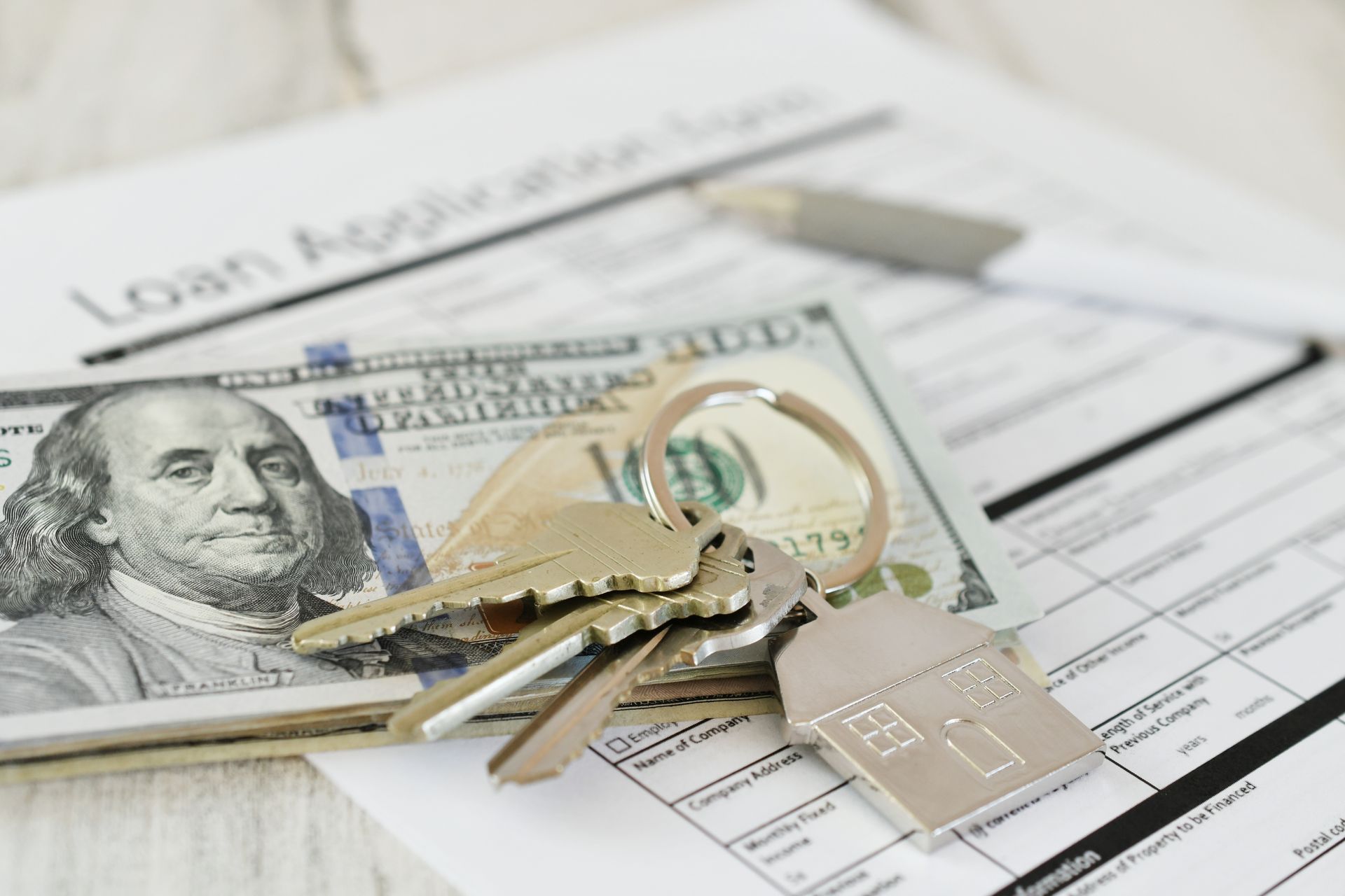 A bunch of keys and money on top of a loan application.