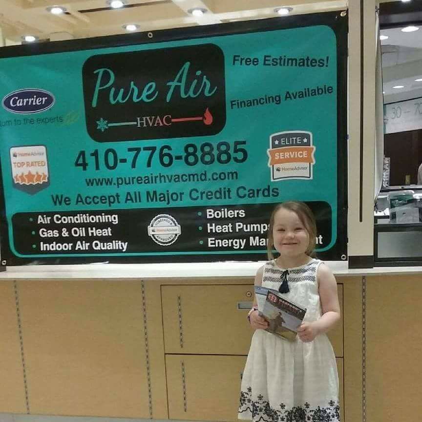 A little girl stands in front of a pure air sign