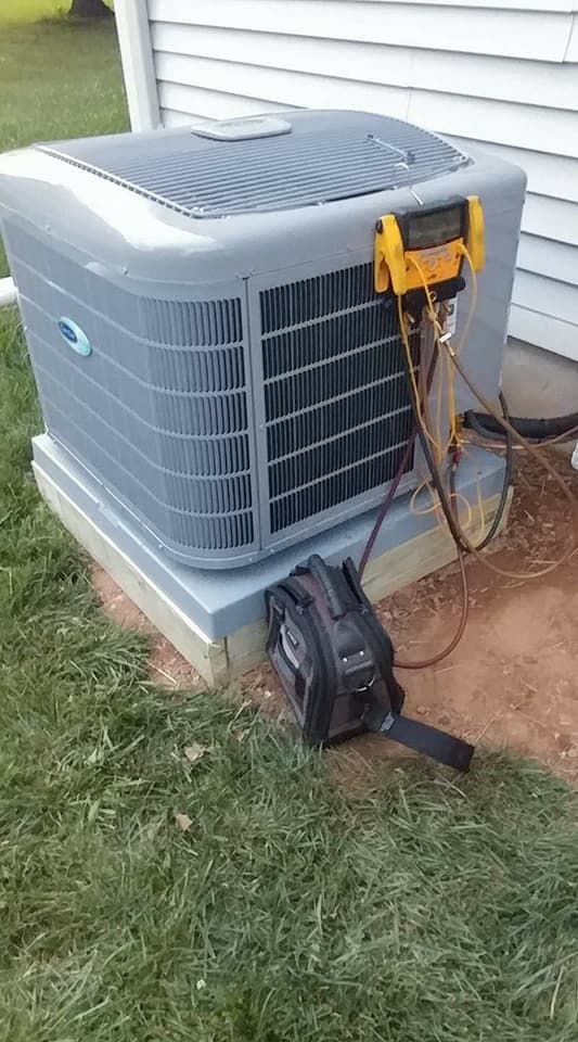 An air conditioner is sitting in the grass next to a house.