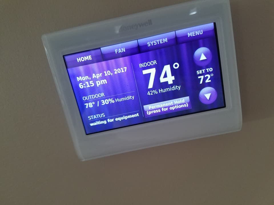 A white thermostat with a purple screen shows the temperature is 74 degrees