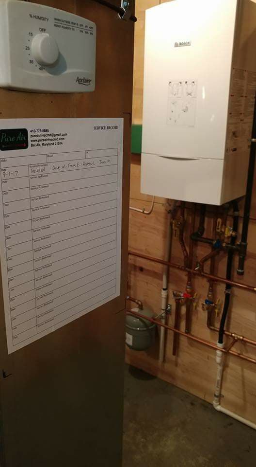 A white boiler is sitting next to a wooden wall in a room.