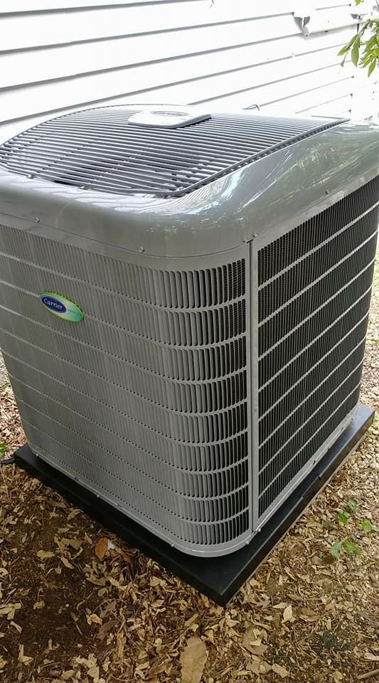 A large air conditioner is sitting on top of a pile of leaves.