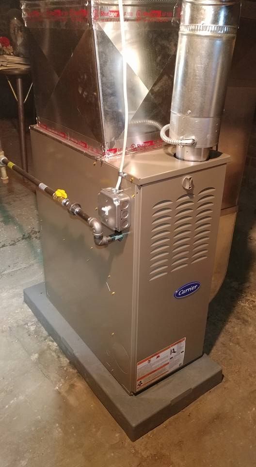 A stainless steel boiler is sitting on top of a concrete base in a basement.