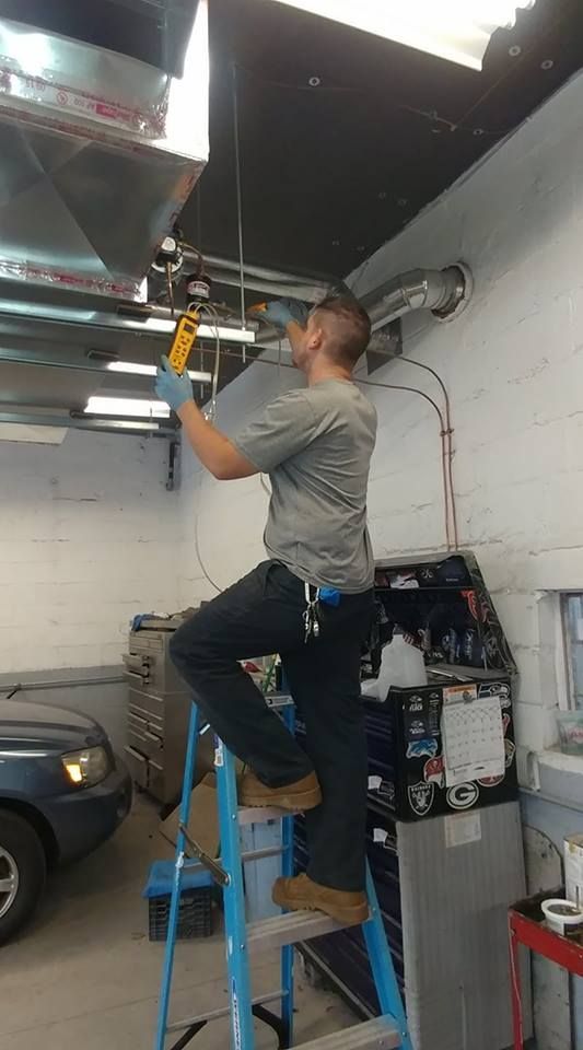 A man is standing on a ladder in a garage working on a ceiling fan.