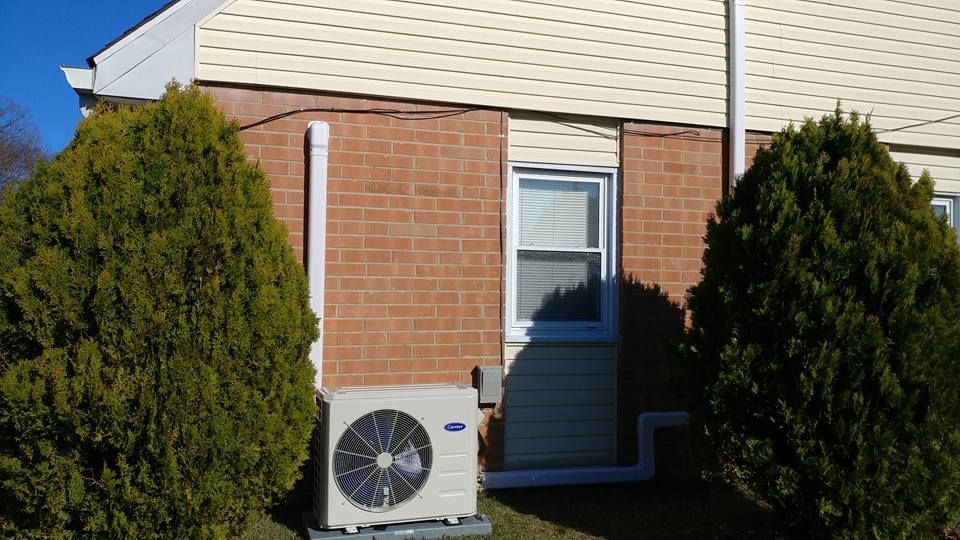 A large air conditioner is sitting outside of a brick building.