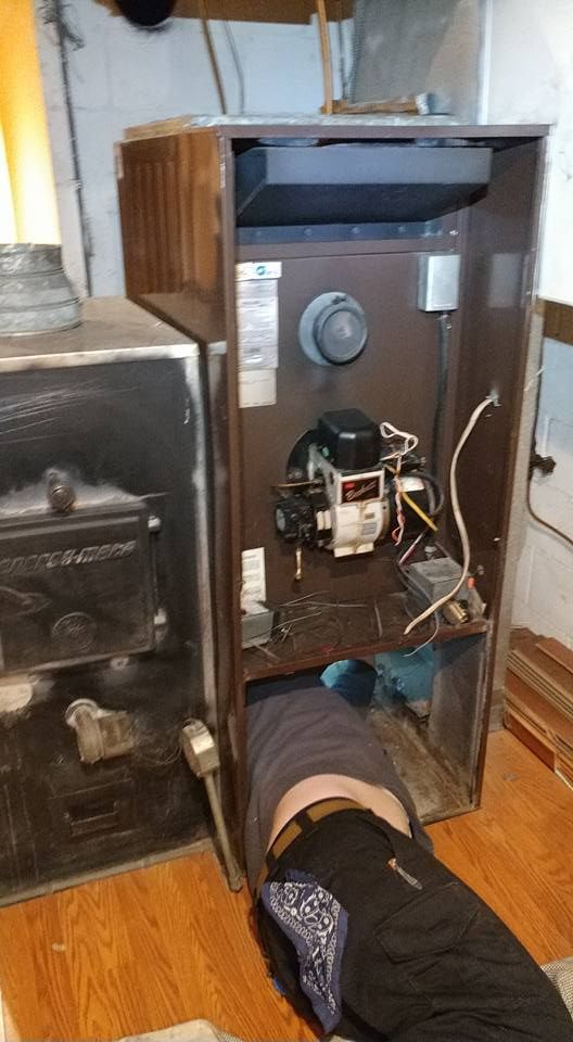A person is kneeling under a heater in a basement.