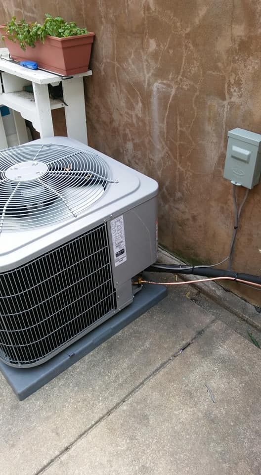 An air conditioner is sitting on the sidewalk next to a wall.