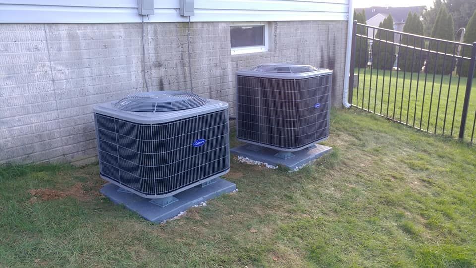 Two air conditioners are sitting on top of a lush green lawn in front of a house.