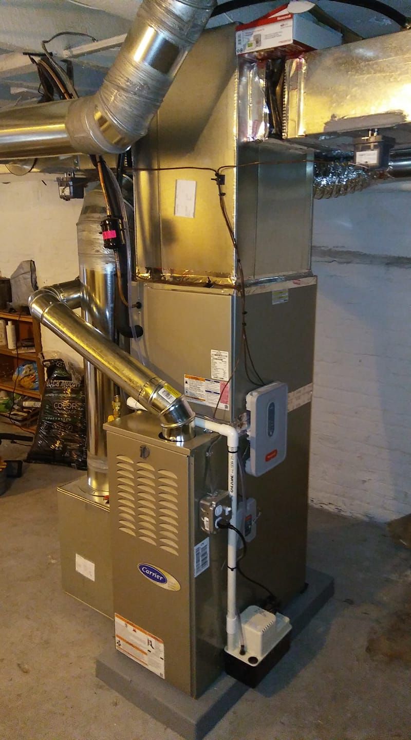 An air conditioner is sitting in a basement next to a chimney.