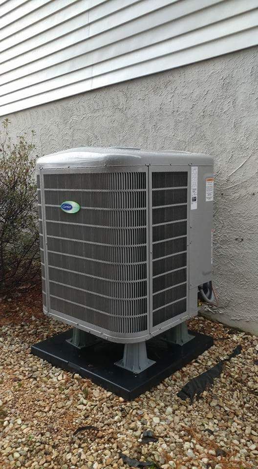 A large air conditioner is sitting on top of a pile of gravel next to a house.
