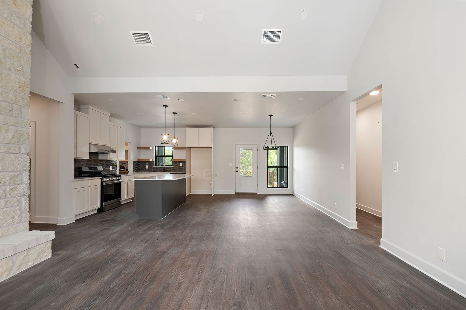 A large empty room with hardwood floors and a kitchen in the background.