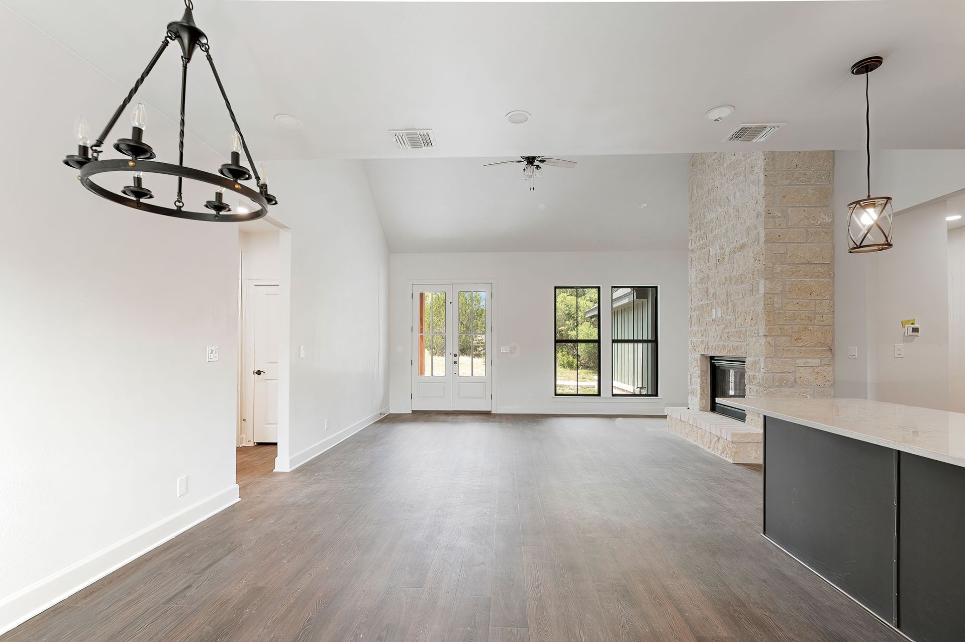 An empty living room with hardwood floors and a chandelier hanging from the ceiling.