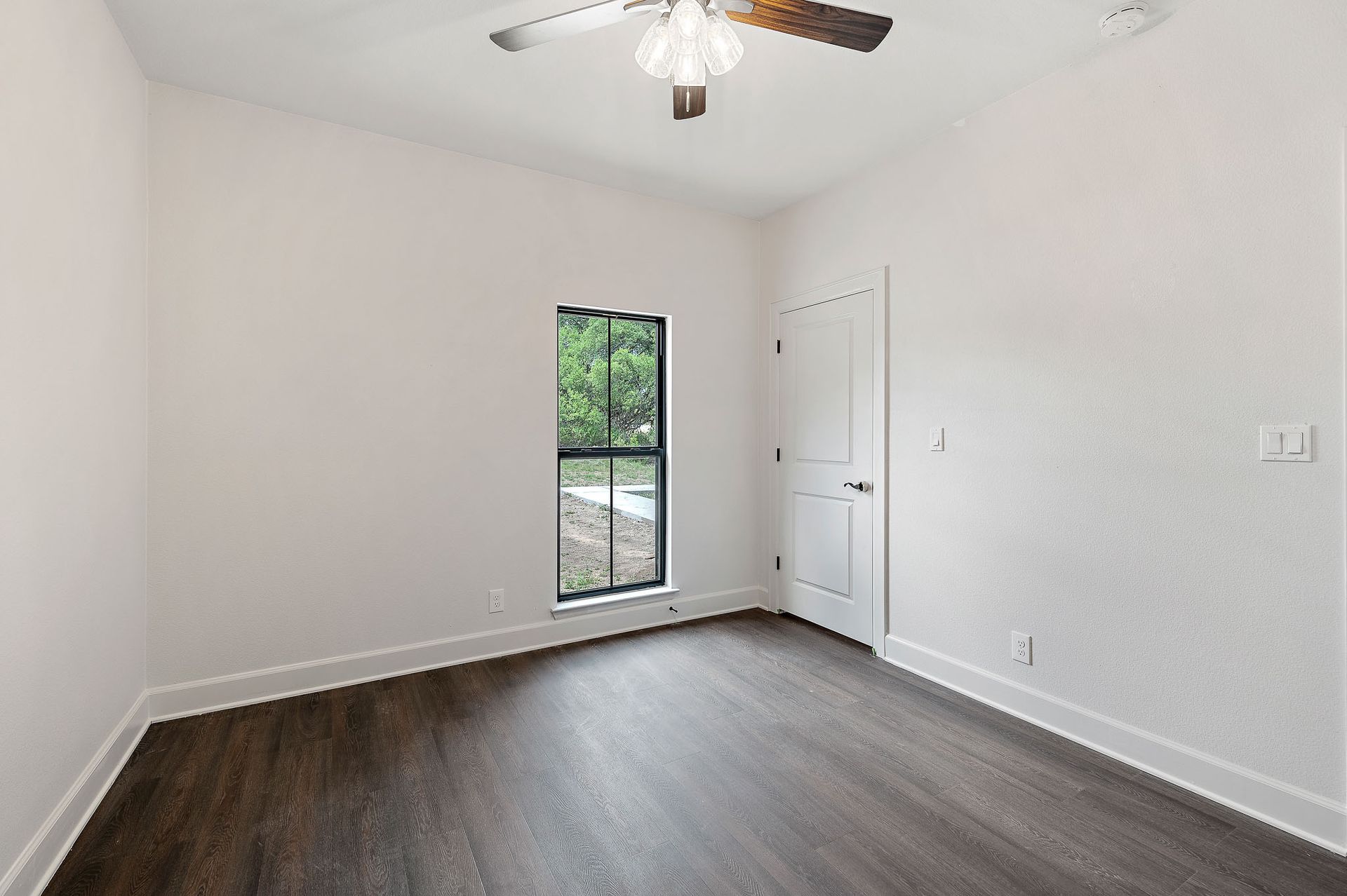 An empty bedroom with a ceiling fan and a window.