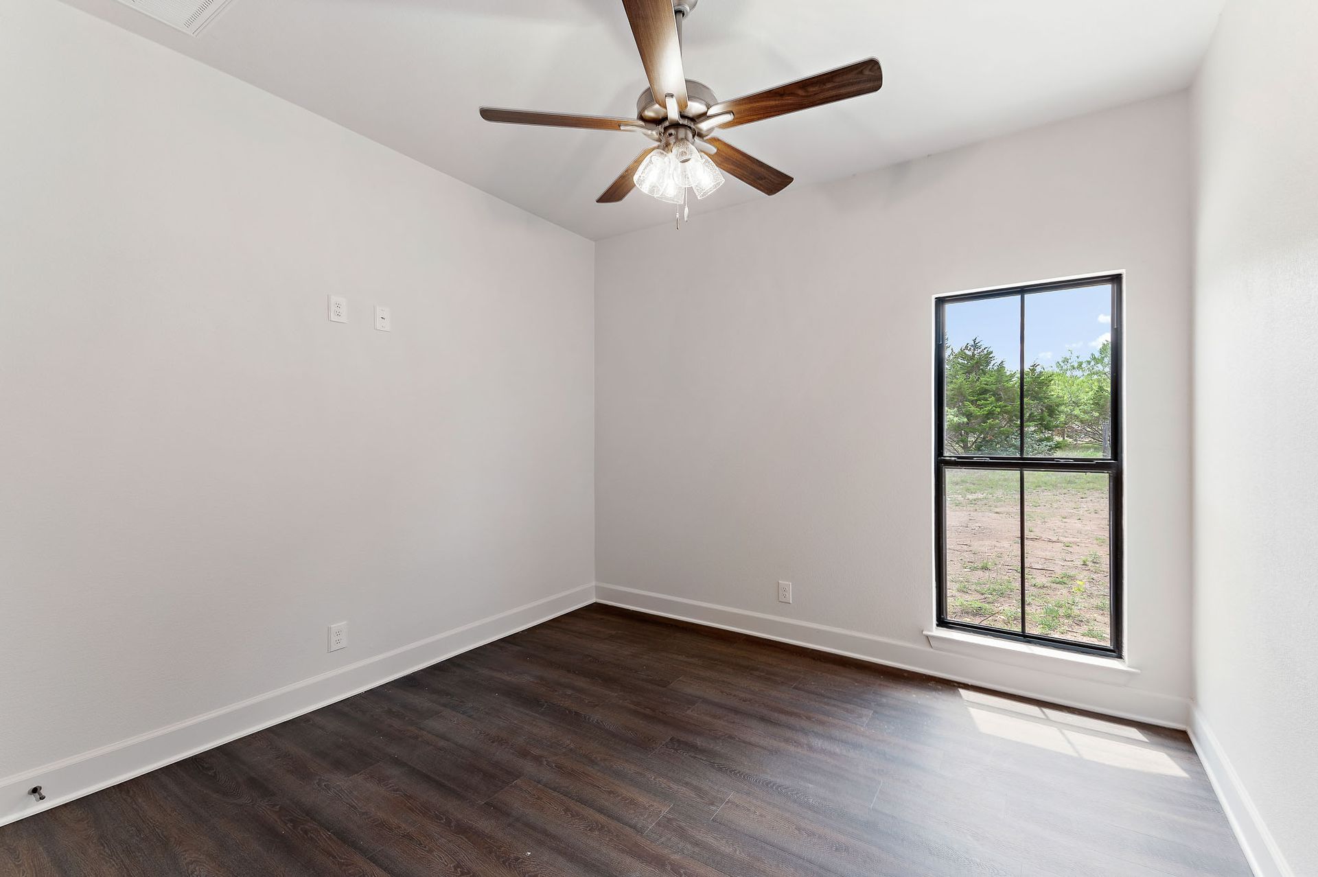 An empty room with a ceiling fan and a window.