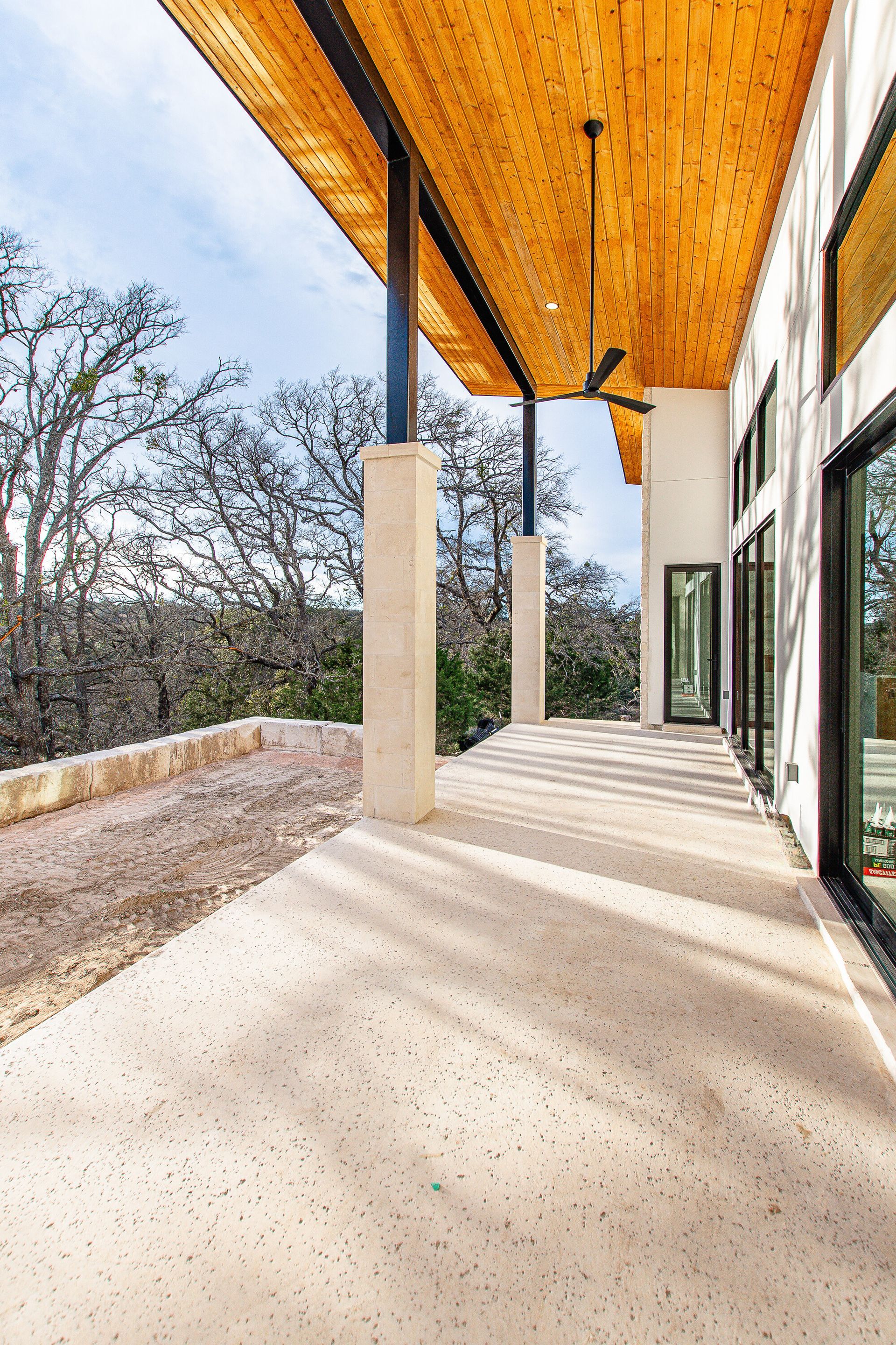 A large covered porch with a wooden ceiling and a ceiling fan.